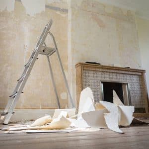 A photo of a room with a fireplace that is currently in the process of being renovated. There are piles of old discarded wallpaper heaped next to a ladder. Your local Pinellas County painter is skilled in completing wall paper removal and painting projects.