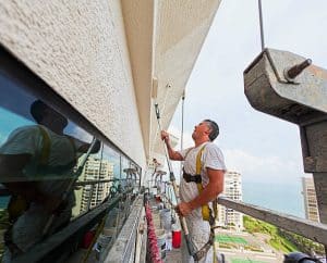 Professional painter wearing a safety harness using a paint roller to paint the exterior of a commercial building in Pinellas County.