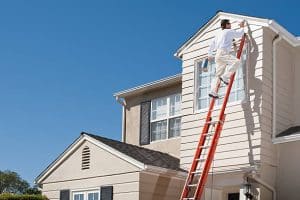 The exterior of a two-story home is being painted by a Pinellas county painting expert on a bright red ladder. 